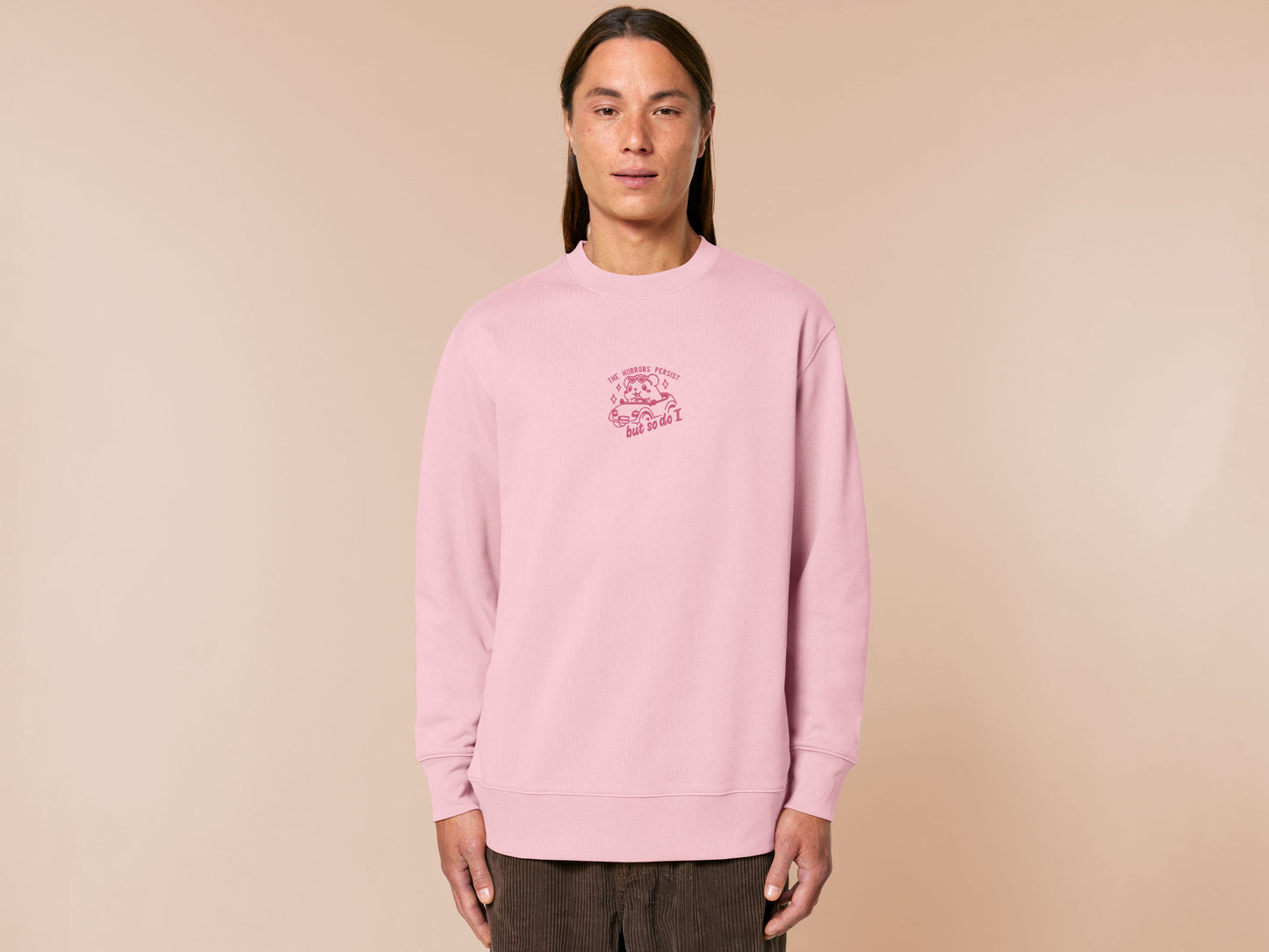 Pink embroidered sweater with a cute chibi guinea pig hamster wearing heart-shaped sunglasses and driving a little pink car surrounded by the quote the horrors persist but so do I.