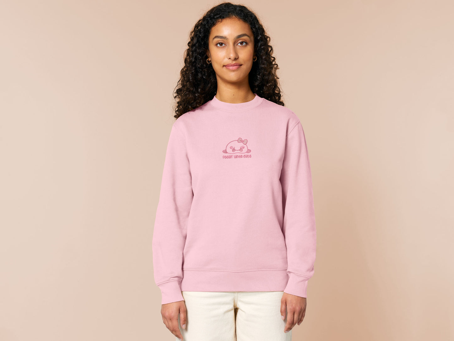 Pink embroidered sweater with a cute chibi blobfish wearing a bow surrounded by the quote feelin kinda cute