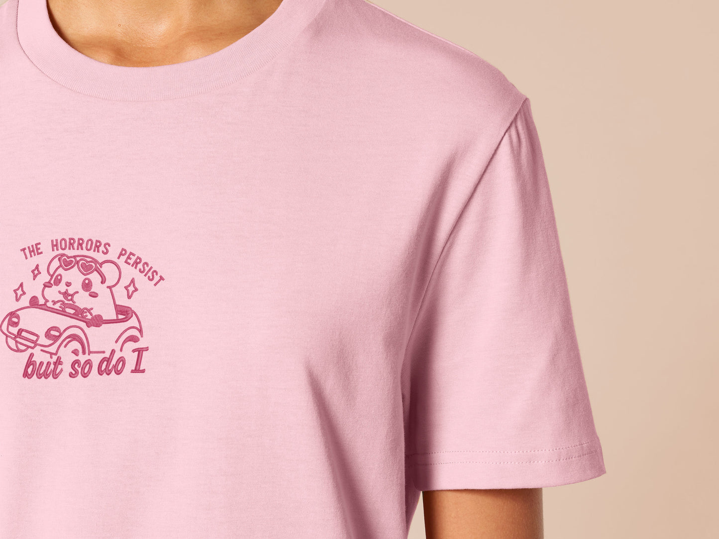 Pink embroidered t-shirt with a cute chibi guinea pig hamster wearing heart-shaped sunglasses and driving a little pink car surrounded by the quote the horrors persist but so do I.