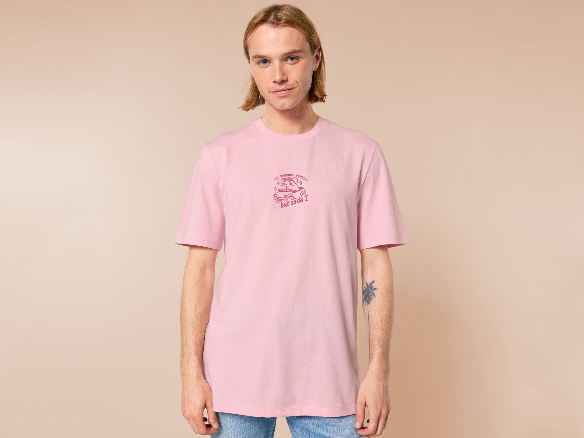 Pink embroidered t-shirt with a cute chibi guinea pig hamster wearing heart-shaped sunglasses and driving a little pink car surrounded by the quote the horrors persist but so do I.