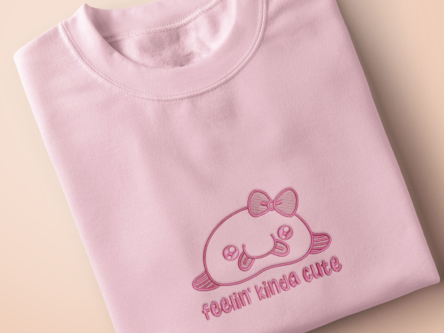 Pink embroidered t-shirt with a cute chibi BLOBFISH wearing a bow surrounded by the quote feelin kinda cute