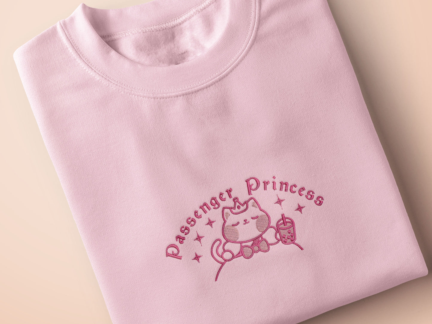 Pink embroidered t-shirt with a cute chibi princess cat wearing a crown and holding a boba tea surrounded by the quote passenger princess