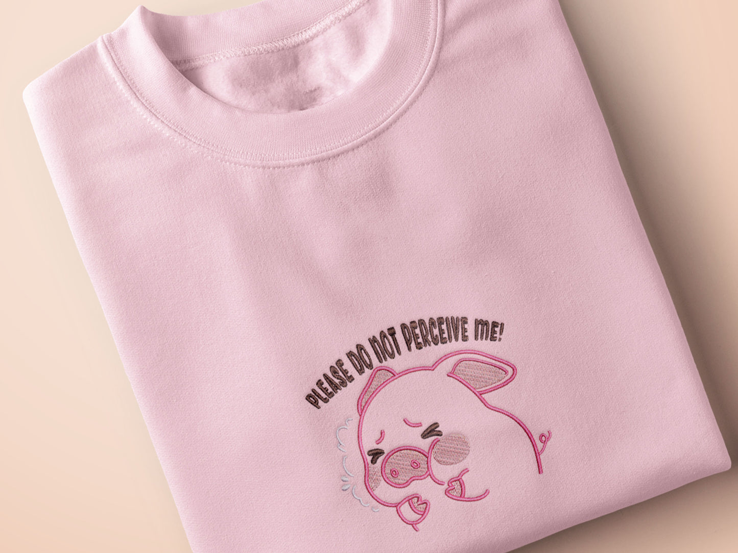 Pink embroidered t-shirt with a cute chibi panicking pig surrounded by the quote please don't perceive me