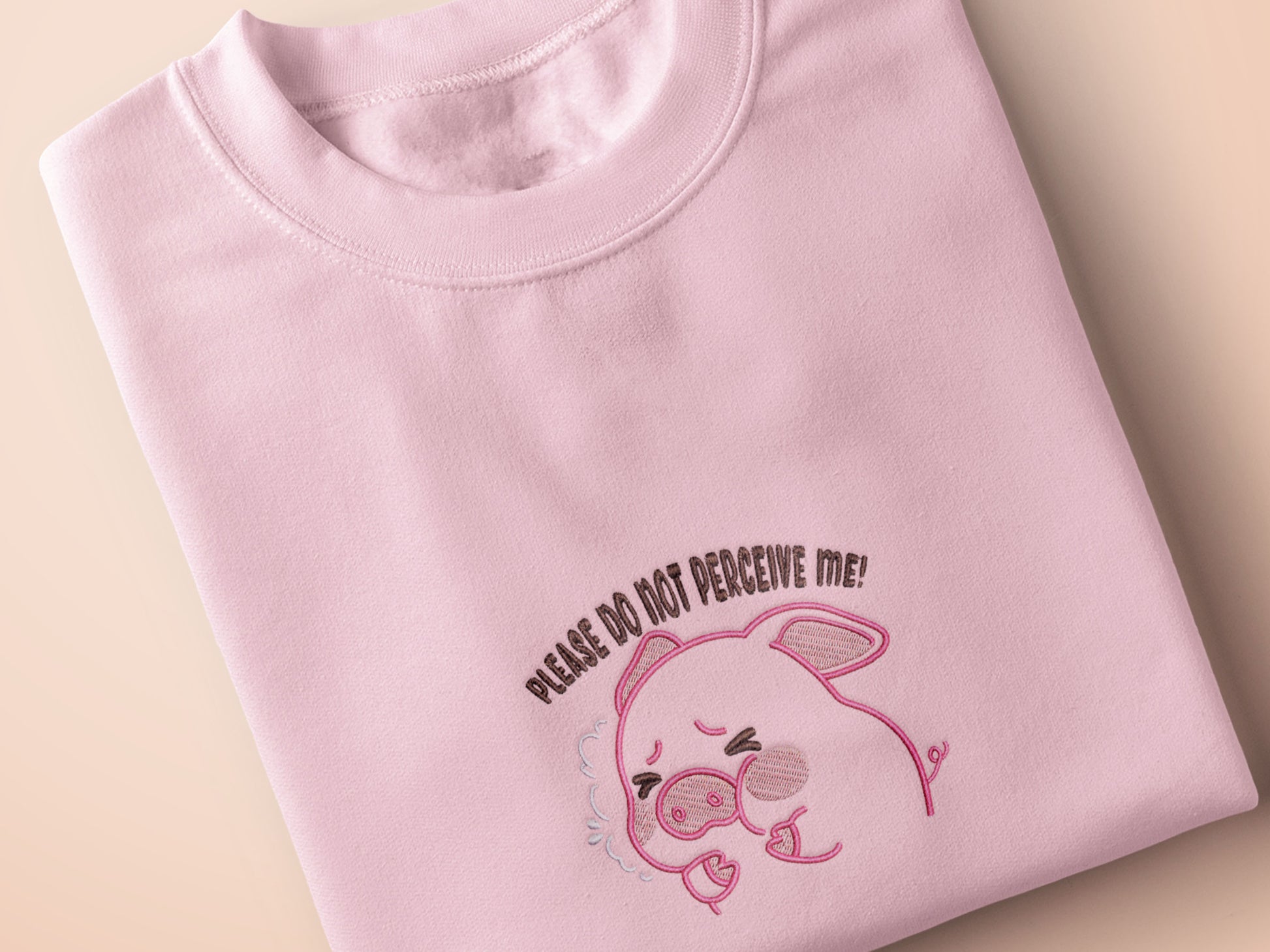 Pink embroidered t-shirt with a cute chibi panicking pig surrounded by the quote please don't perceive me
