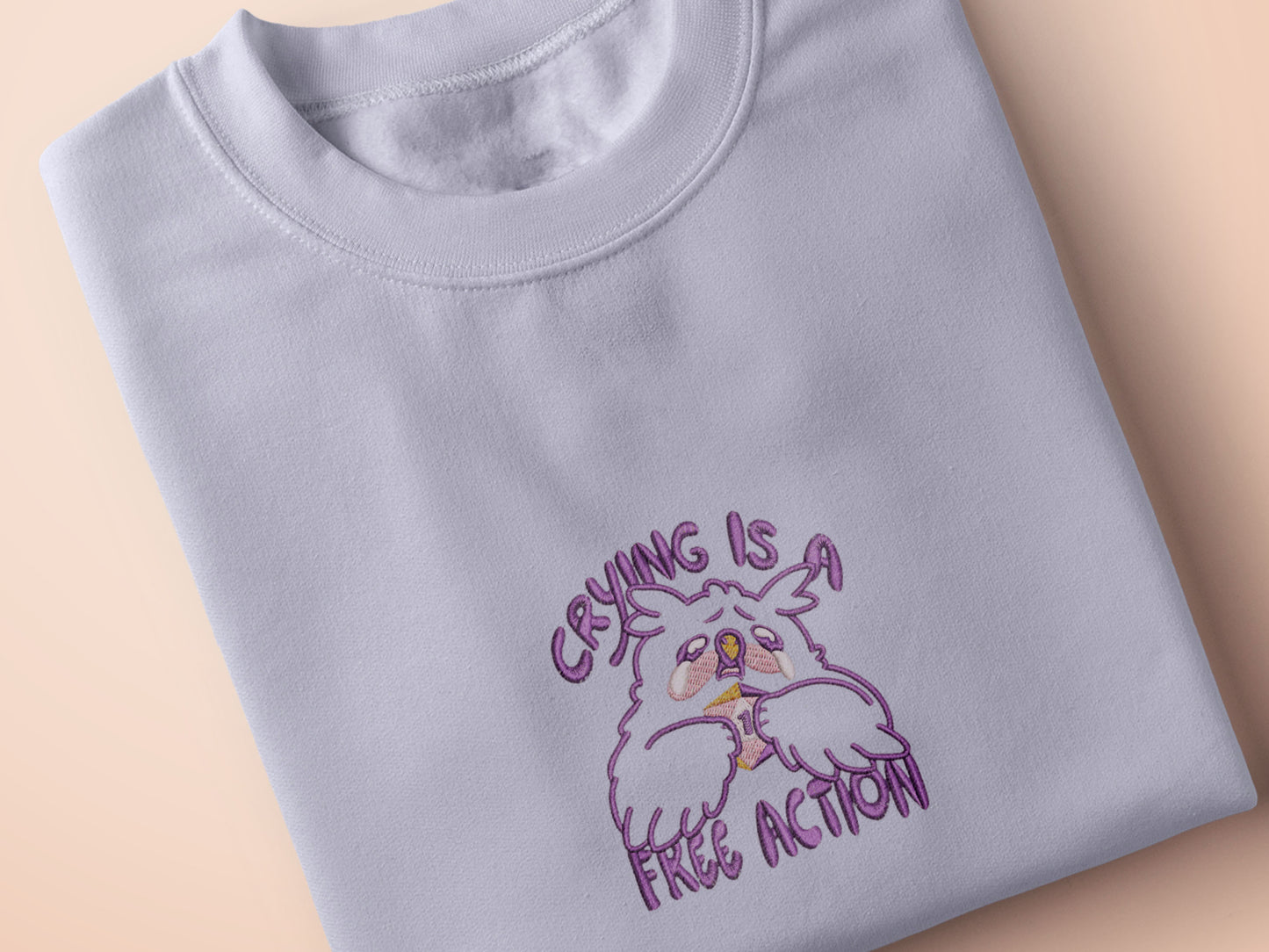 Purple embroidered cute design of a chibi owlbear crying holding a d20 dice that has rolled a one with the quote Crying Is A Free Action
