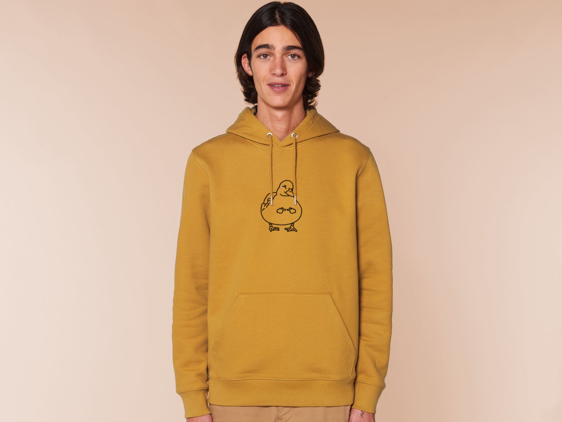 A man wearing a yellow long sleeve fleece hoodie, with an embroidered black thread design of cute blushing duck with the for me finger hand emoji symbols