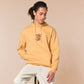 A yellow hoodie with an embroidered design of a cute grumpy red dragon playing a card game with the text why is it not my turn yet?!