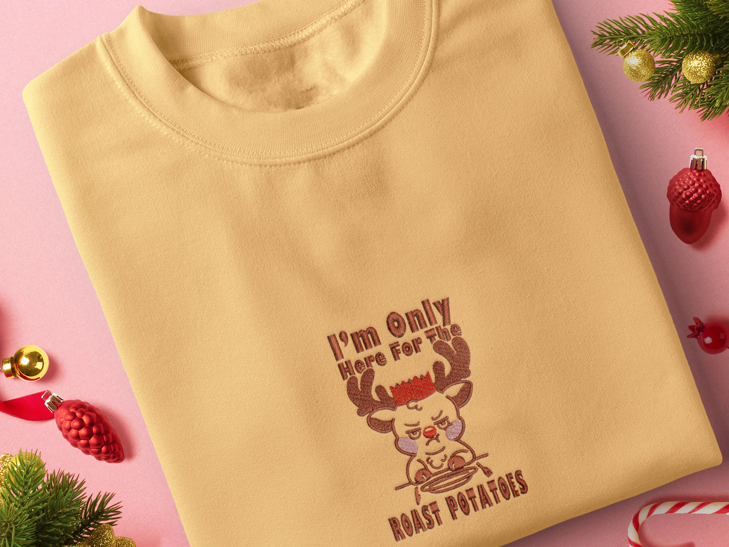 A yellow crew neck long sleeve sweater, with an embroidered design of a cute sulking Rudolph reindeer and the quote I'm only here for the roast potatoes