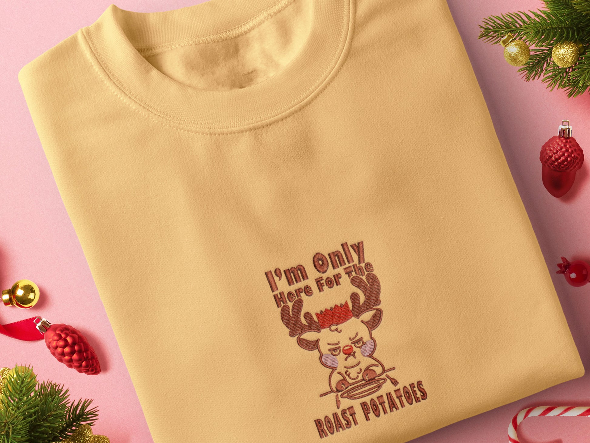 A yellow crew neck long sleeve sweater, with an embroidered design of a cute sulking Rudolph reindeer and the quote I'm only here for the roast potatoes