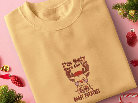 A yellow crew neck long sleeve sweater, with an embroidered design of a cute sulking Rudolph reindeer and the quote I'm only here for the roast potatoes
