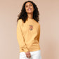 A yellow sweater with an embroidered design of a cute grumpy red dragon playing a card game with the text why is it not my turn yet?!