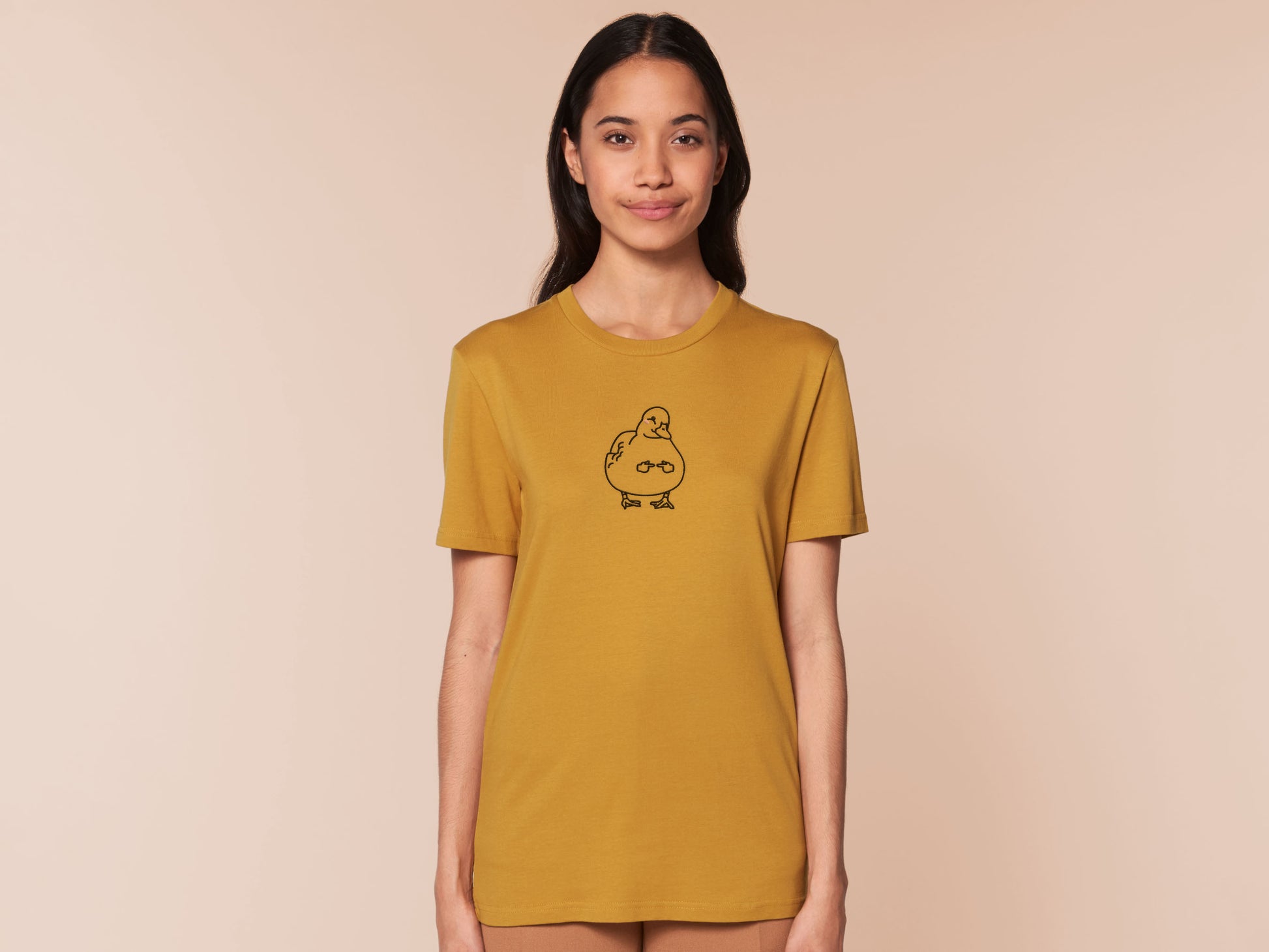 A woman wearing a yellow crew neck short sleeve t-shirt, with an embroidered black thread design of cute blushing duck with the for me finger hand emoji symbols
