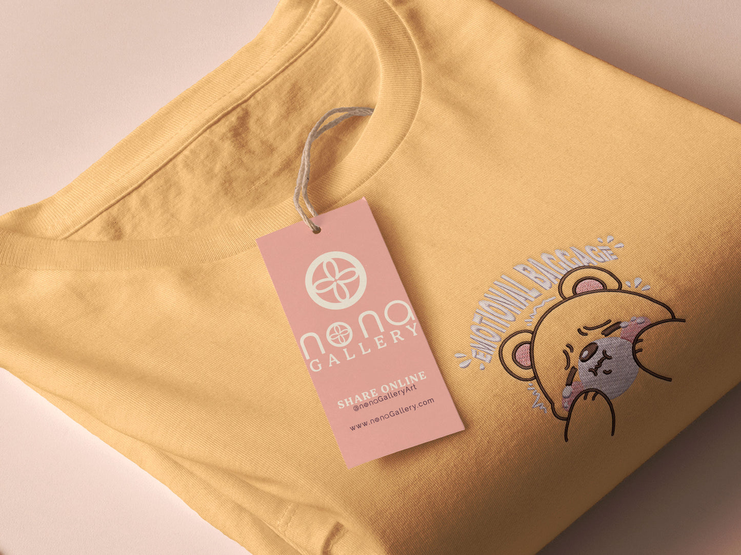A yellow crew neck short sleeve t-shirt, with an embroidered brown thread design of a cute panicking bear and the quote emotional baggage