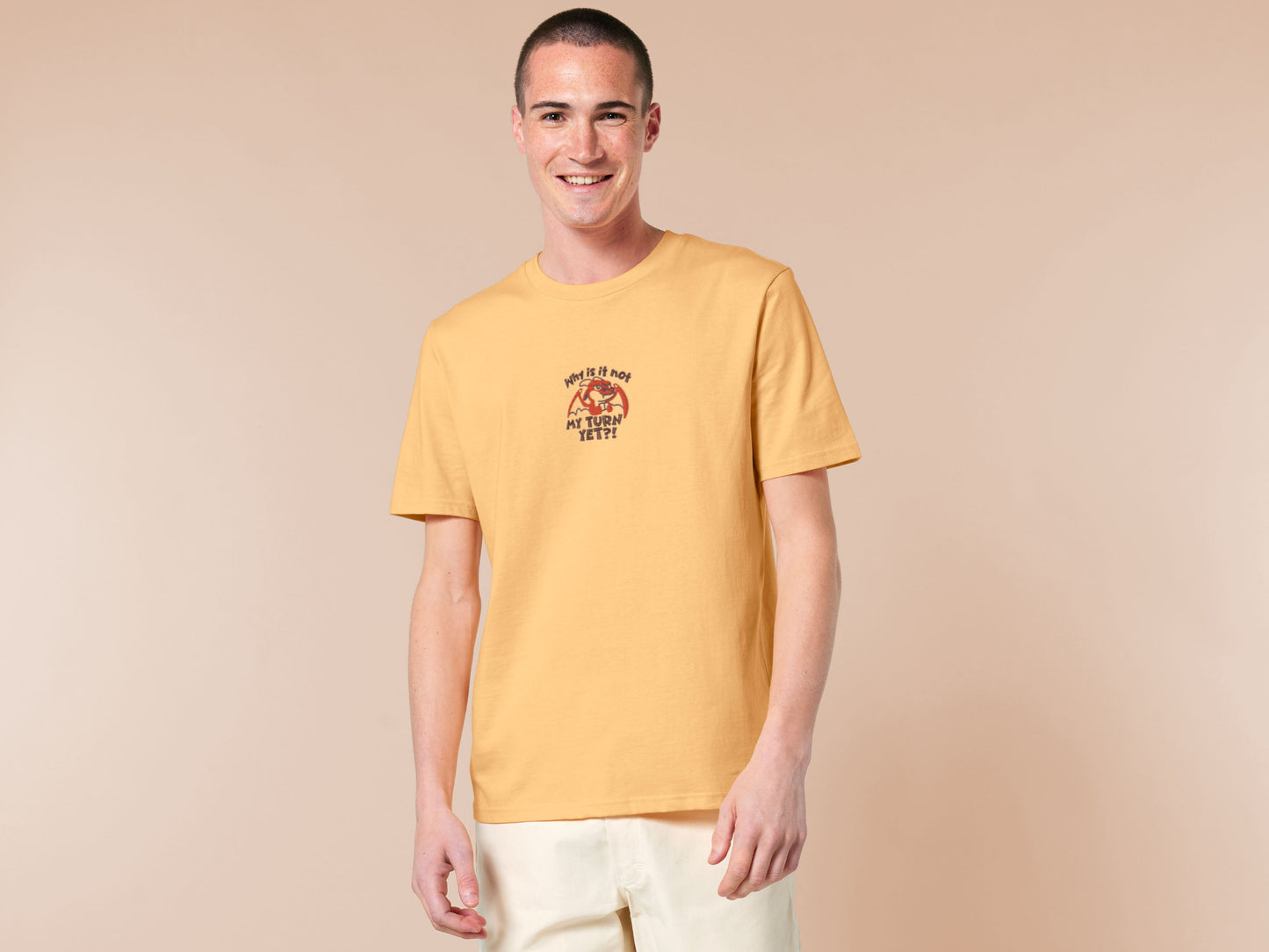 A yellow tshirt with an embroidered design of a cute grumpy red dragon playing a card game with the text why is it not my turn yet?!