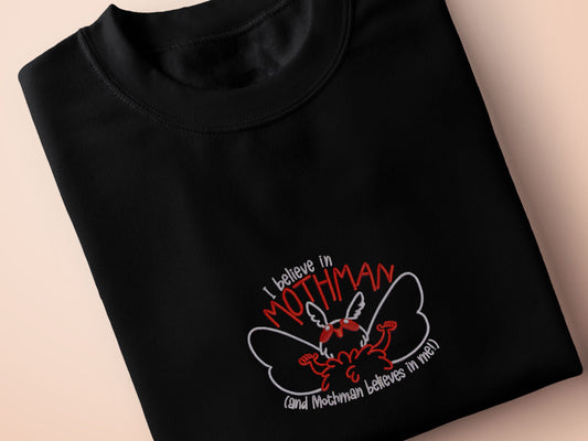 Embroidered black t-shirt with a cute chibi cryptid design of Mothman with the text I believe in Mothman (and Mothman believes in me!)