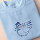 An embroidered blue t-shirt design of a cute pigeon wearing a top hat and the text It's Called Fashion Susan