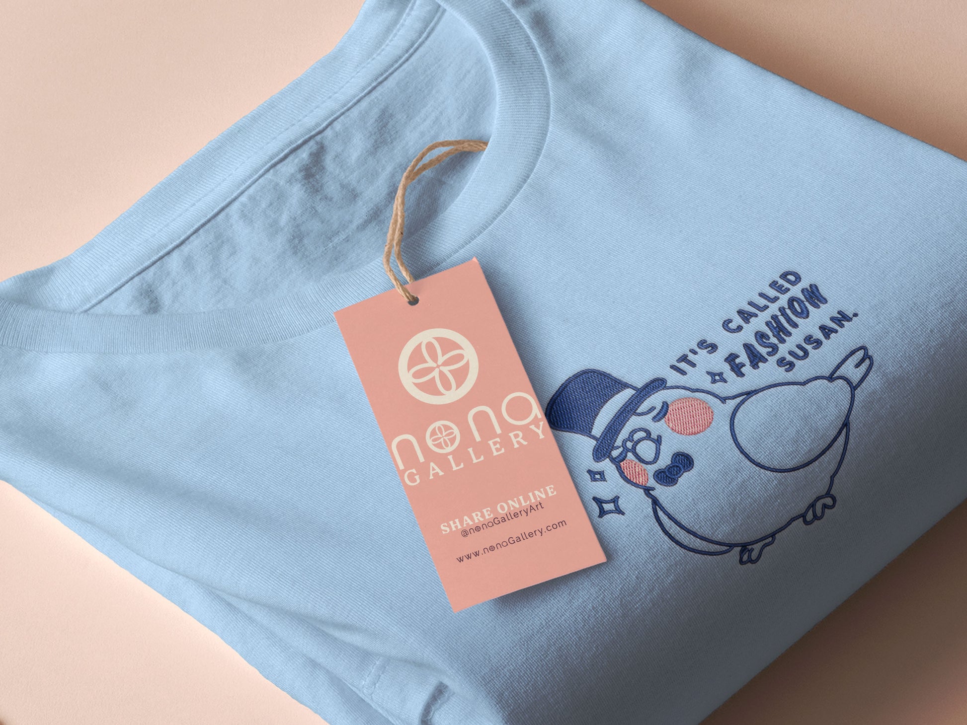 An embroidered blue t-shirt design of a cute pigeon wearing a top hat and the text It's Called Fashion Susan