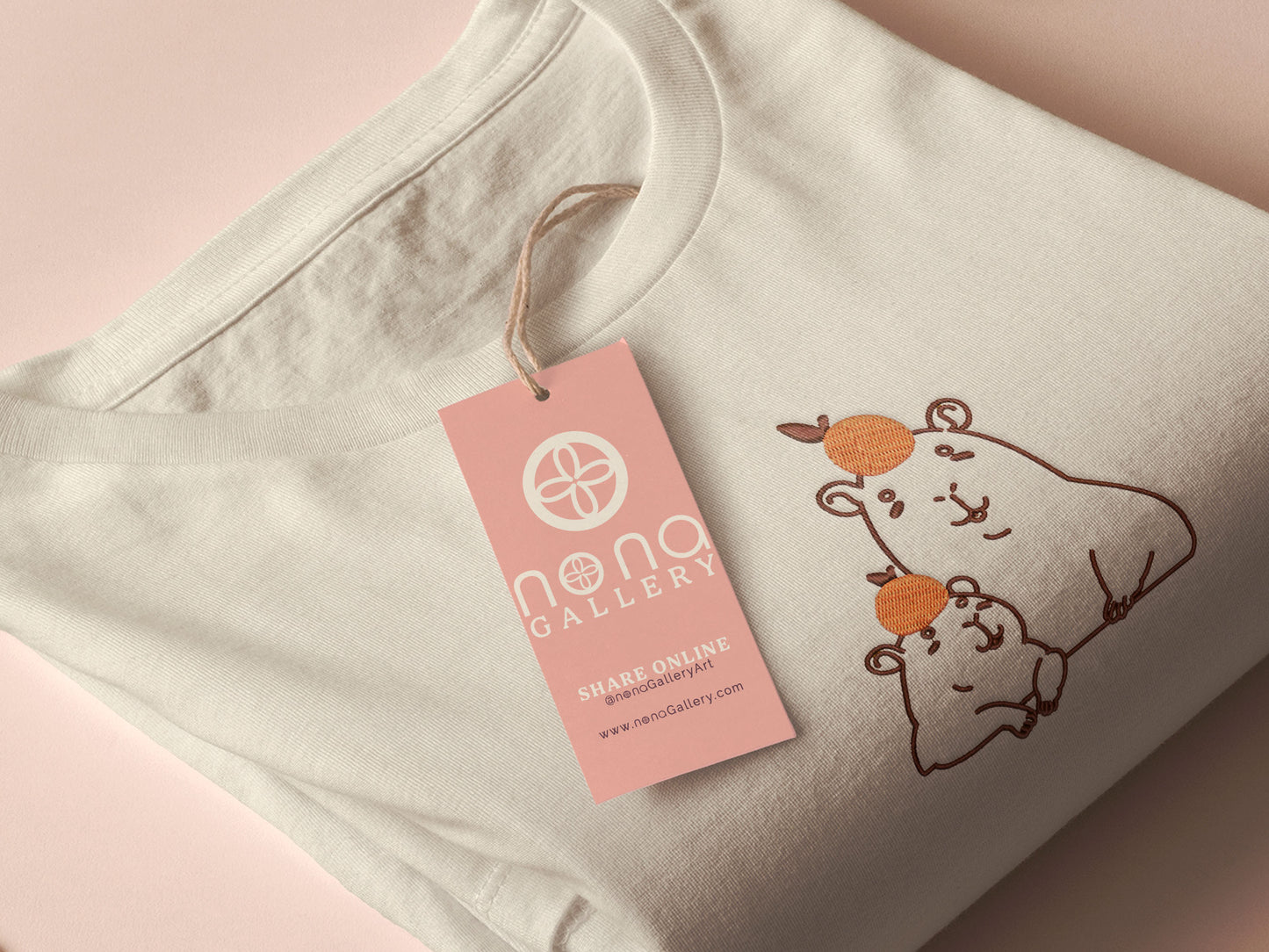 Embroidered cream t-shirt design of two cute chibi capybaras with oranges on their heads.