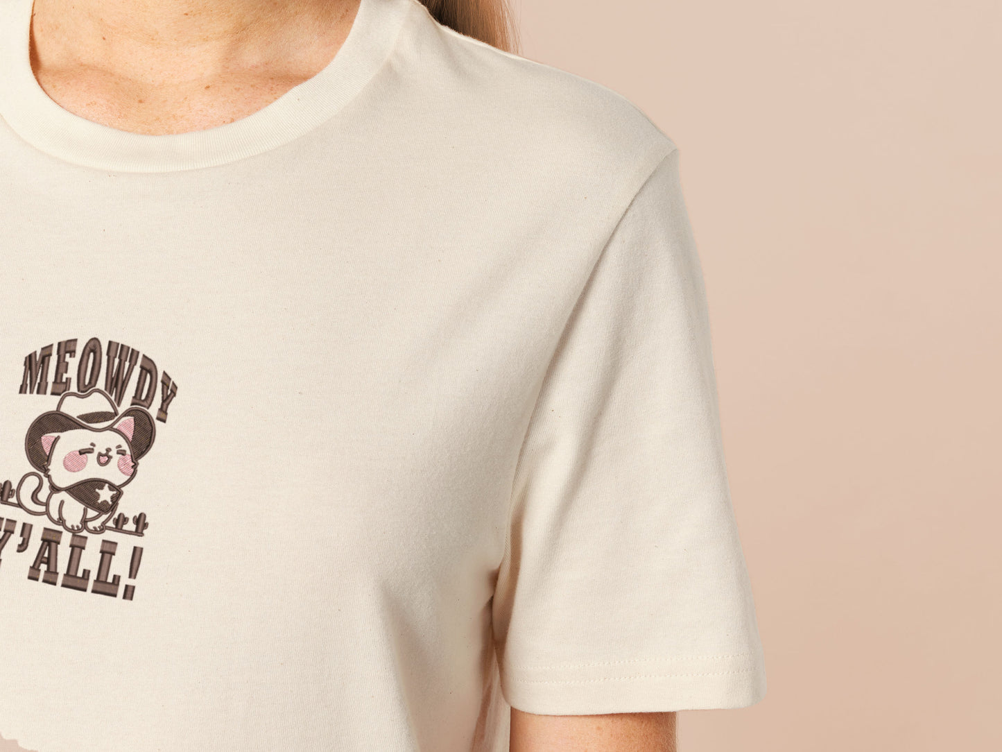 A cream crew neck short sleeve t-shirt, with an embroidered brown thread design of a cute cowboy cat with hat surrounded by the quote meowfy ya'll!