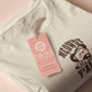 A cream crew neck short sleeve t-shirt, with an embroidered brown thread design of a cute cowboy cat with hat surrounded by the quote meowfy ya'll!