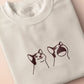 A cream crew neck short sleeve t-shirt, with an embroidered brown thread design of a cute popcat the cat meme reaction twitch emote