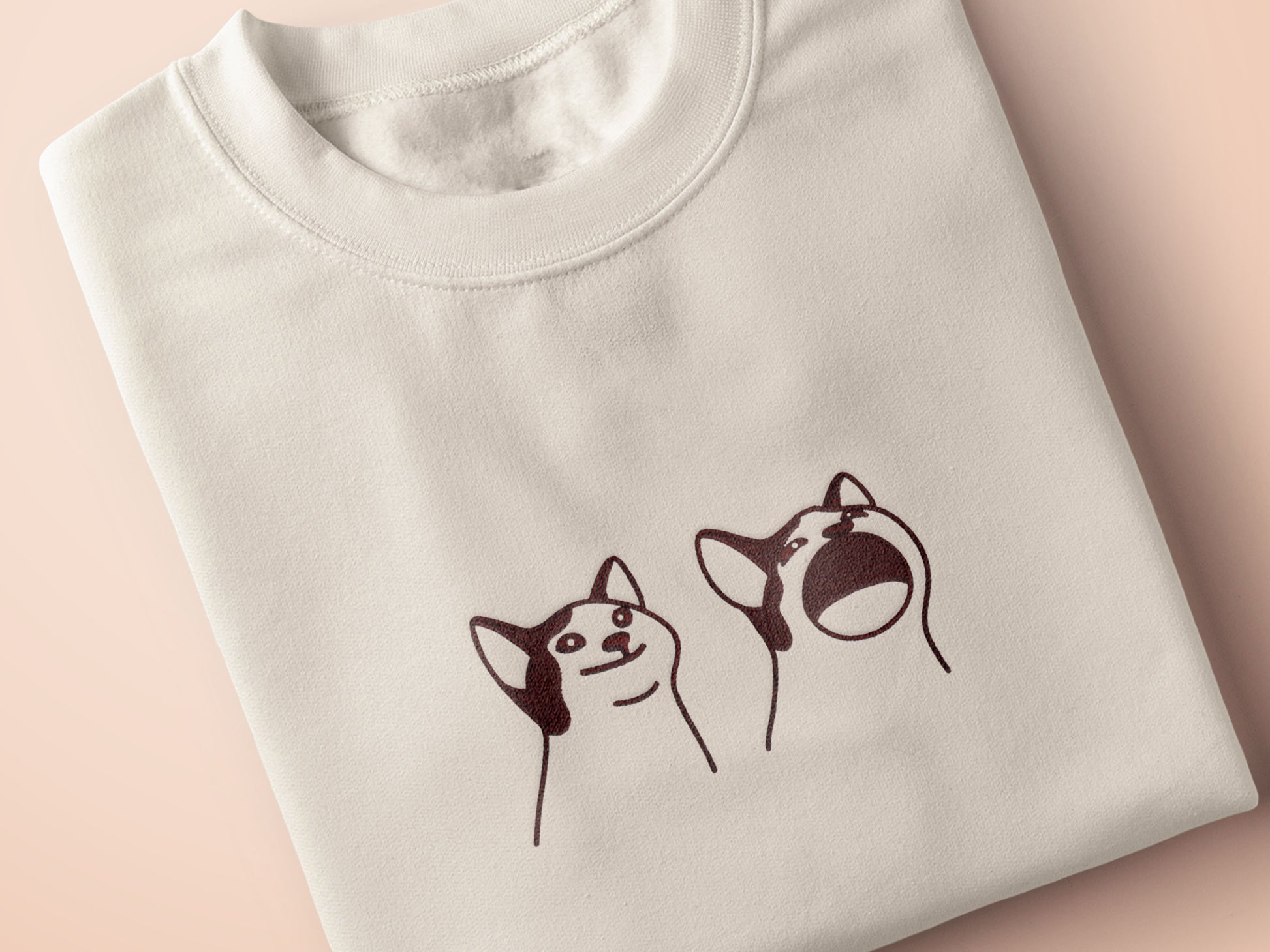 A cream crew neck short sleeve t-shirt, with an embroidered brown thread design of a cute popcat the cat meme reaction twitch emote