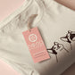 A cream crew neck short sleeve t-shirt, with an embroidered brown thread design of a cute popcat the cat meme reaction twitch emote