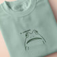 An embroidered green t-shirt design of a funny cartoon frog with the text a concern.