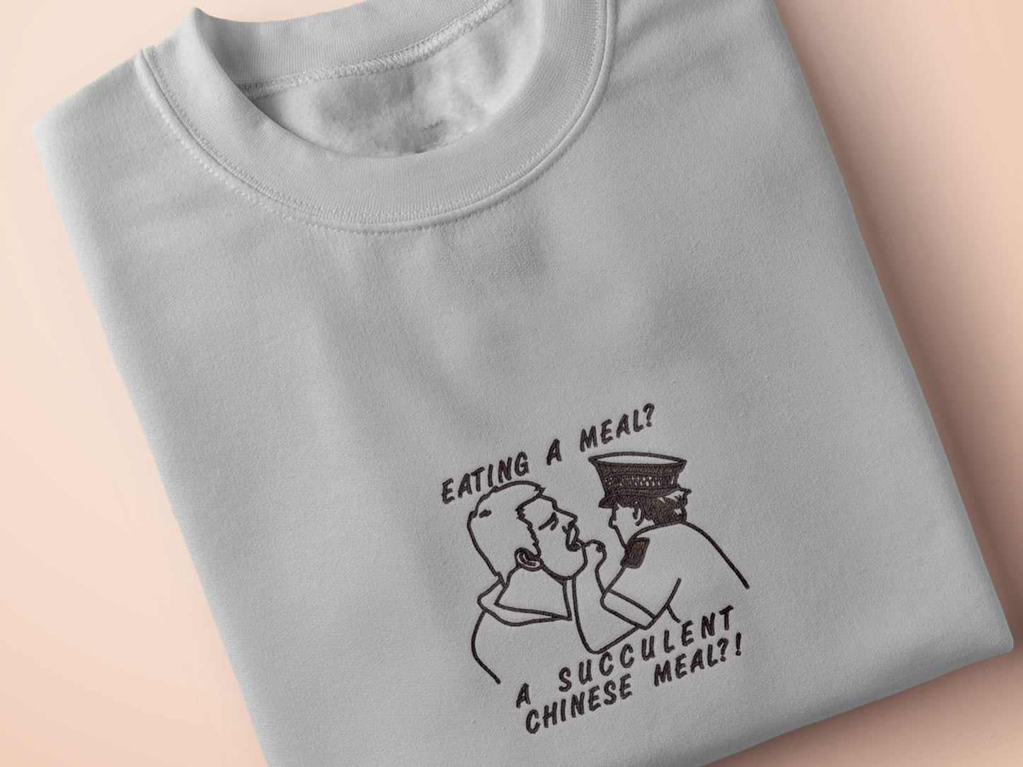 An embroidered light grey t-shirt design of the Australian Jack Karlson being arrested while he shouts Eating A Meal? A Succulent Chinese Meal?!