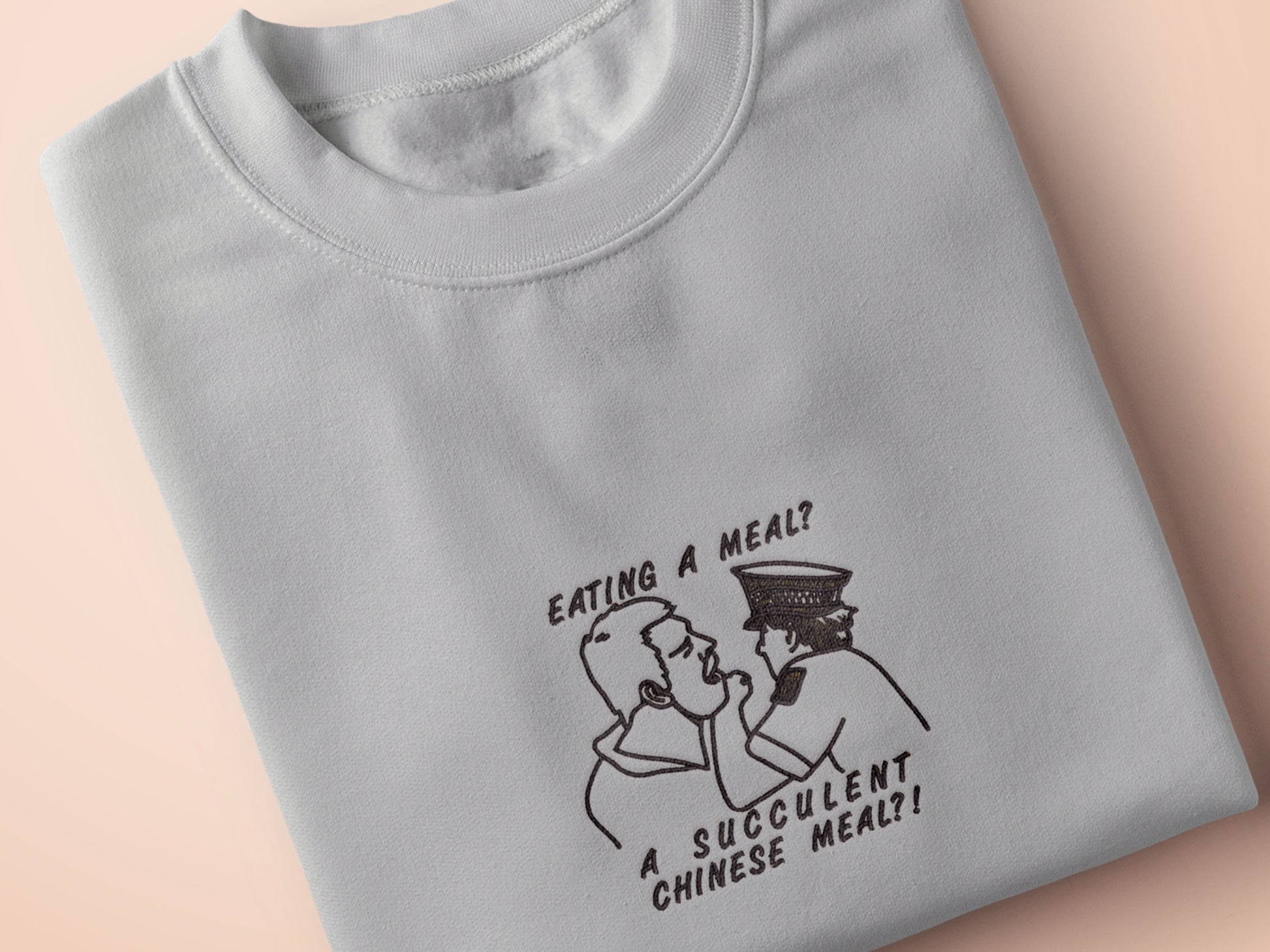 An embroidered light grey t-shirt design of the Australian Jack Karlson being arrested while he shouts Eating A Meal? A Succulent Chinese Meal?!