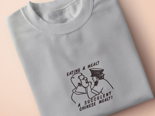 An embroidered light grey t-shirt design of the Australian Jack Karlson being arrested while he shouts Eating A Meal? A Succulent Chinese Meal?!