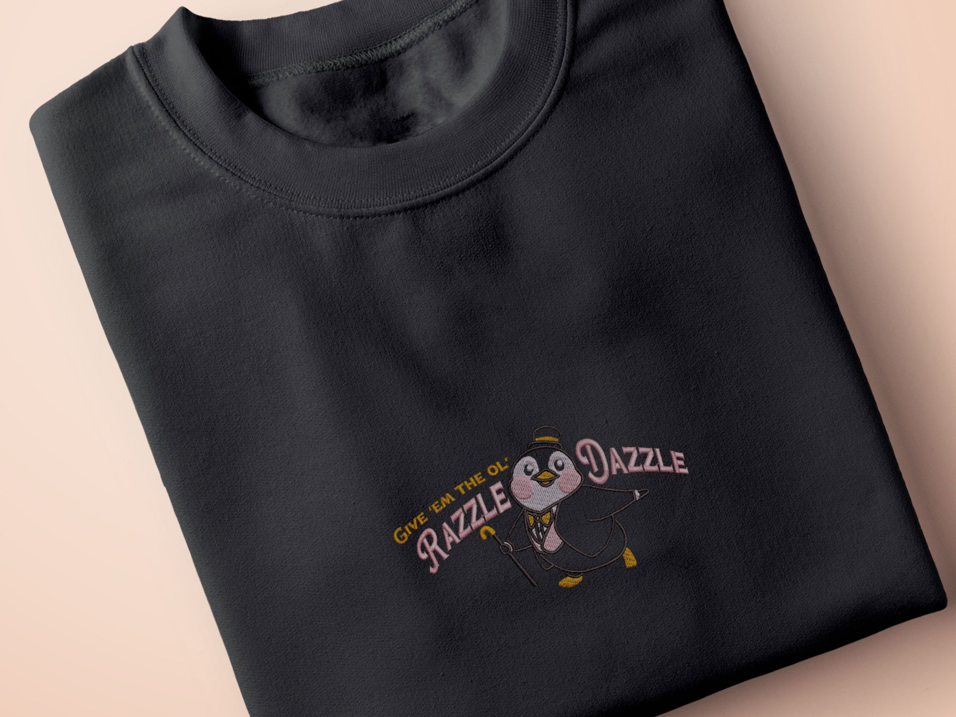 A grey crew neck short sleeve t-shirt, with an embroidered penguin in a fancy suit and top hat and the quote Give 'em the ol' Razzle Dazzle.