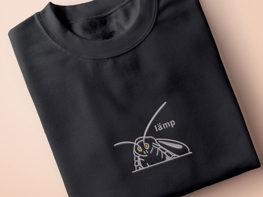 A grey crew neck short sleeve t-shirt, with an embroidered Mothman white thread design of a moth with glowing yellow eyes and the word lämp