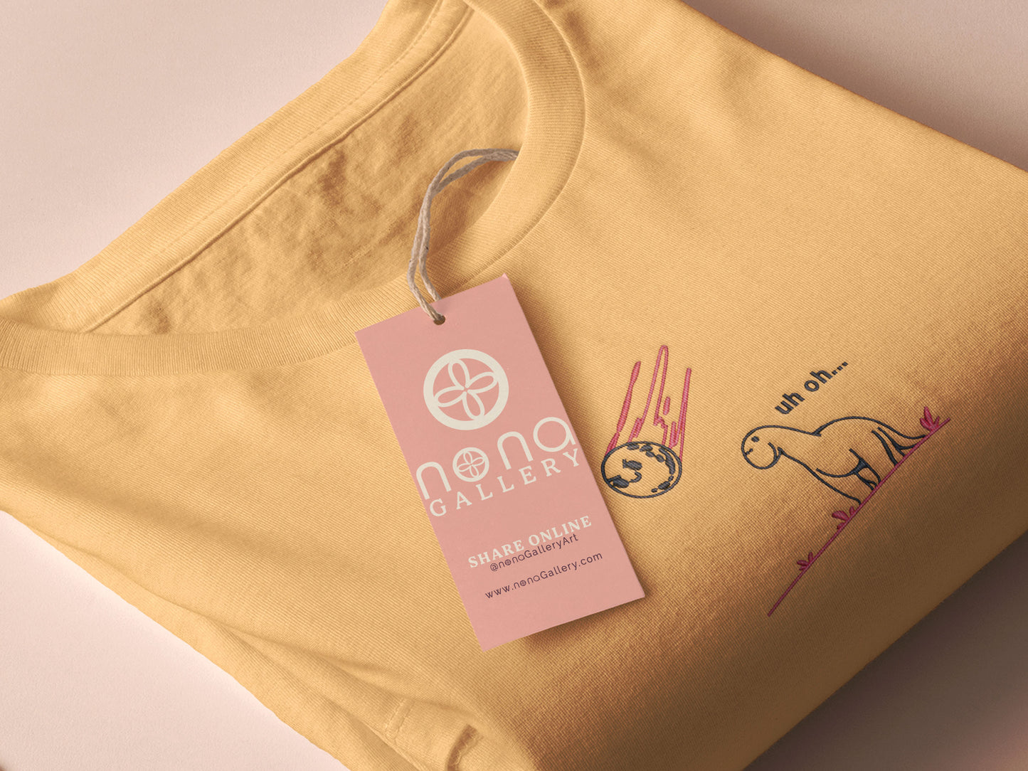 A yellow top with a blue and pink embroidered design of a cute smiling dinosaur looking at a meteor plummeting to earth with the text uh oh...