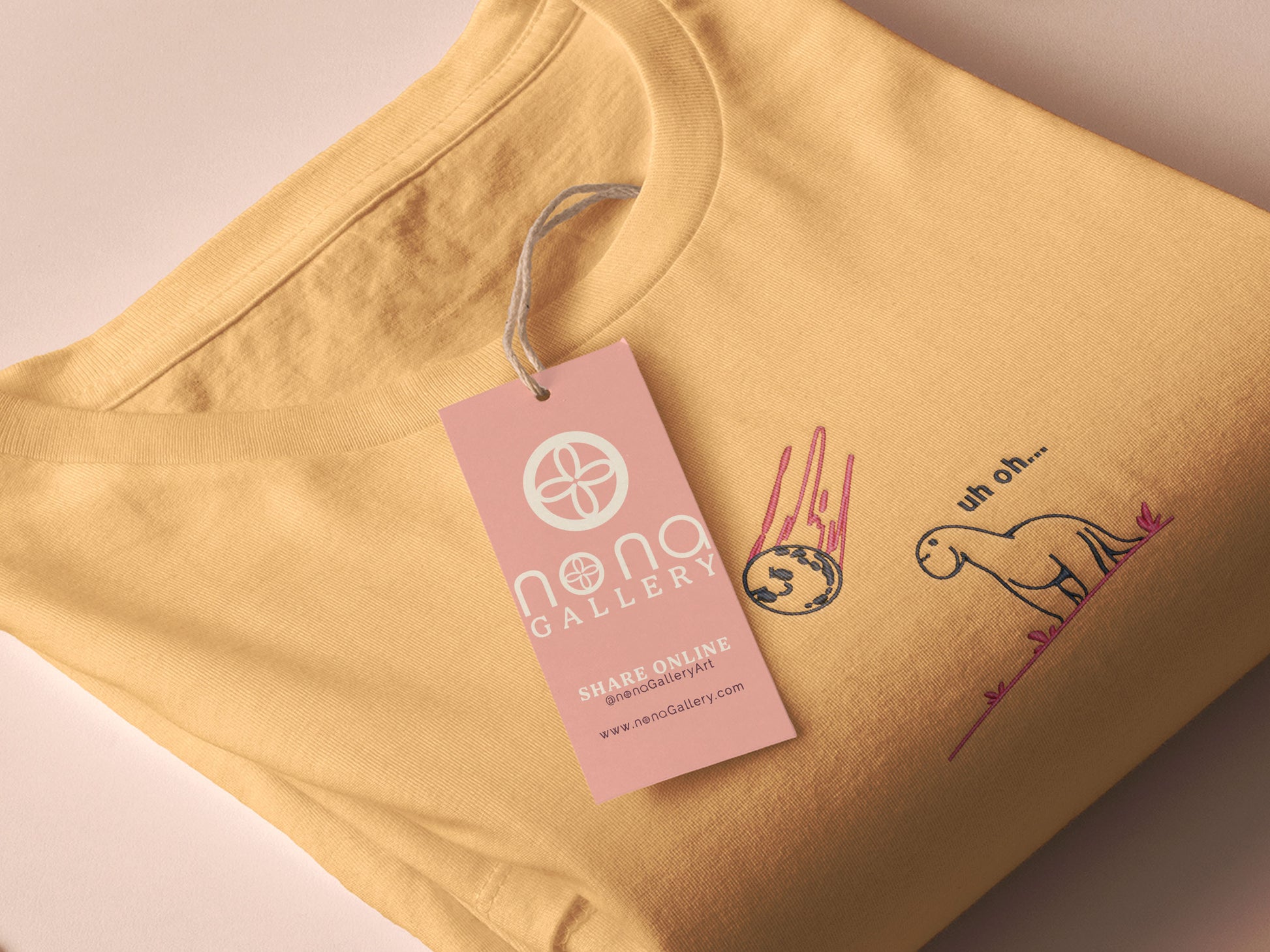 A yellow top with a blue and pink embroidered design of a cute smiling dinosaur looking at a meteor plummeting to earth with the text uh oh...