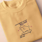 Light yellow short sleeve t-shirt with embroidered pink and blue design of a cute chibi skateboarding cat with the text some people are just too cool but not me.