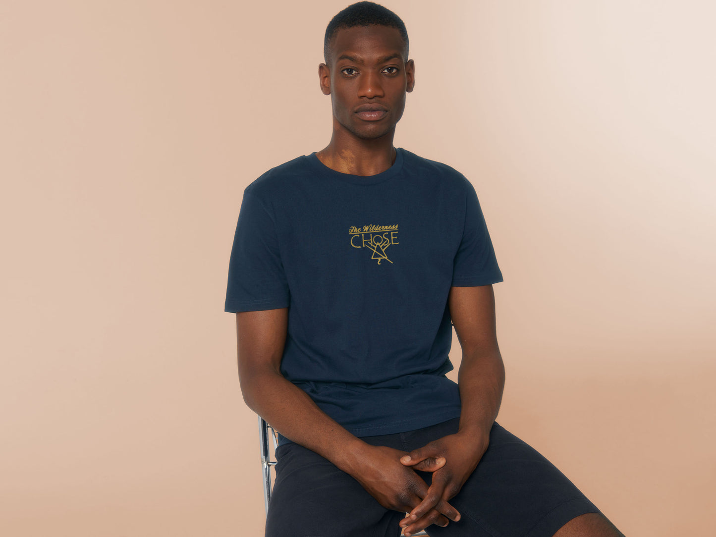 An embroidered yellow design on a navy t-shirt with the quote The Wilderness chose, featuring the cult symbol from the TV show Yellowjackets