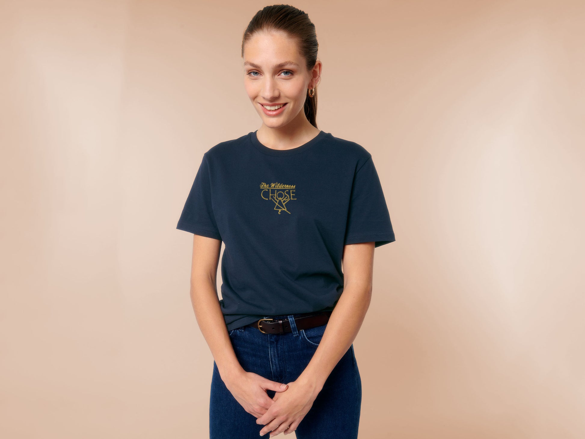 An embroidered yellow design on a navy t-shirt with the quote The Wilderness chose, featuring the cult symbol from the TV show Yellowjackets