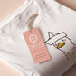 An embroidered white t-shirt design of a cute cartoon goose wearing a paper hat with text underneath that reads you silly goose.