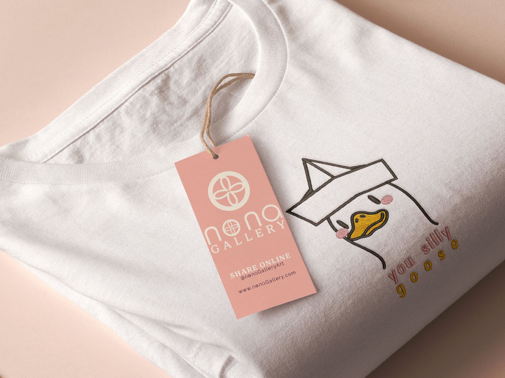 An embroidered white t-shirt design of a cute cartoon goose wearing a paper hat with text underneath that reads you silly goose.