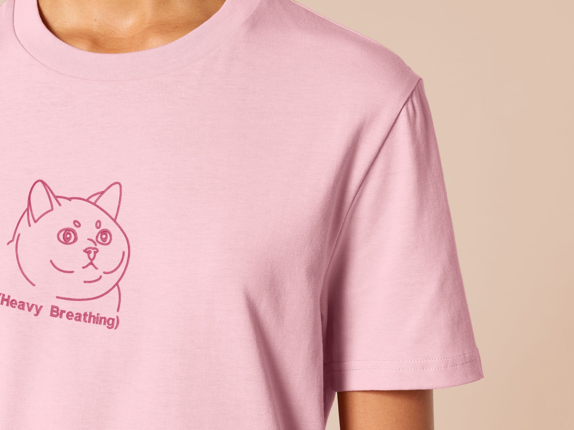 A pink crew neck short sleeve t-shirt, with an embroidered pink thread design of a cute fat cat portrait with text underneath saying (Heavy Breathing)