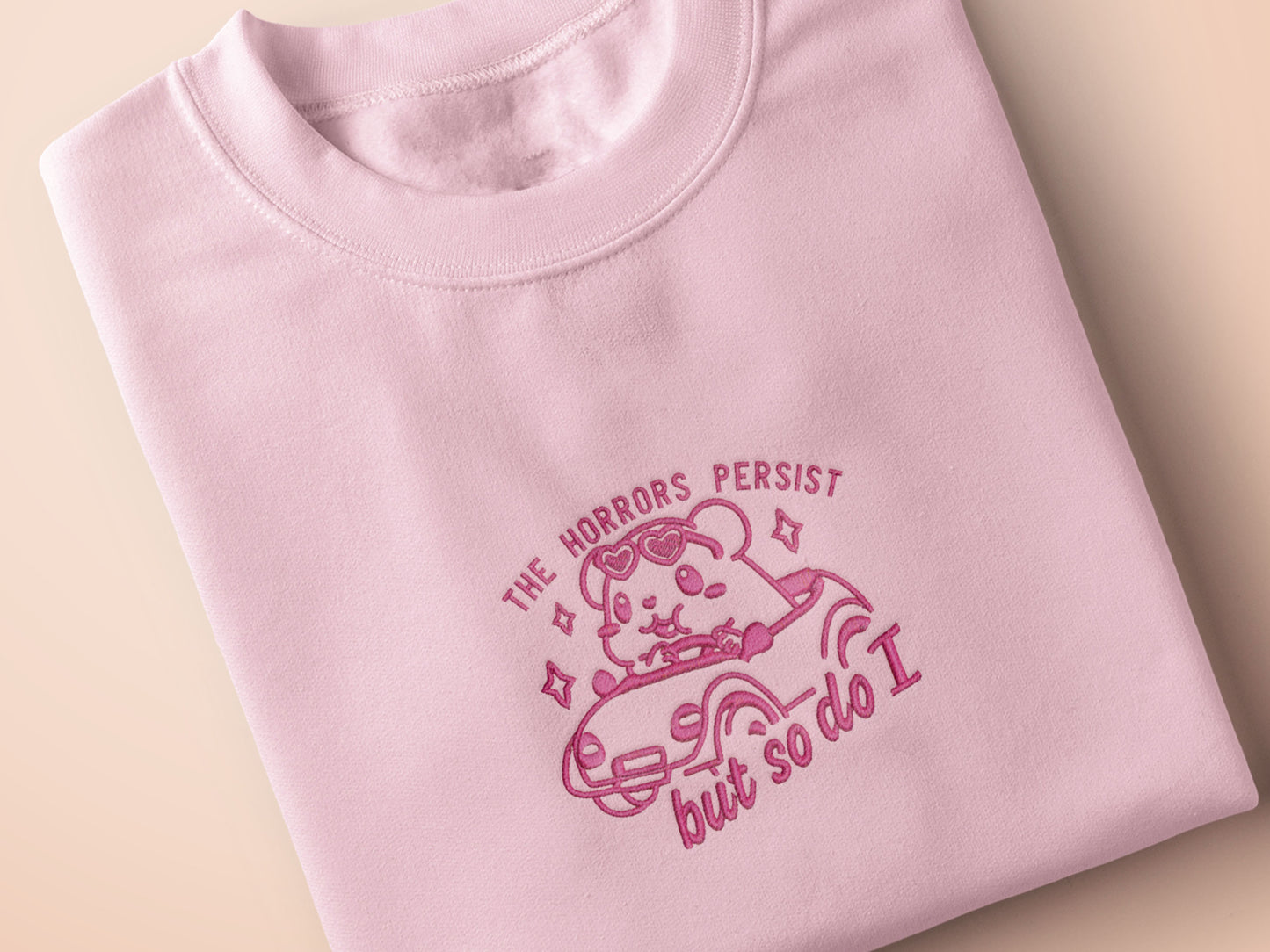 Pink embroidered t-shirt with a cute chibi guinea pig hamster wearing heart-shaped sunglasses and driving a little pink car surrounded by the quote the horrors persist but so do I.