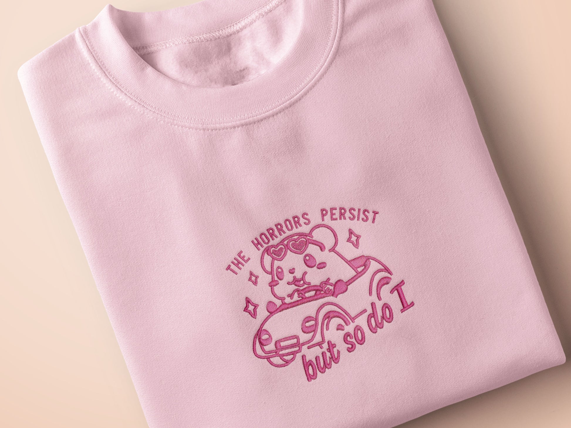 Pink embroidered t-shirt with a cute chibi guinea pig hamster wearing heart-shaped sunglasses and driving a little pink car surrounded by the quote the horrors persist but so do I.