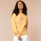 A yellow crew neck long sleeve sweater, with an embroidered brown thread design of a cute panicking bear and the quote emotional baggage