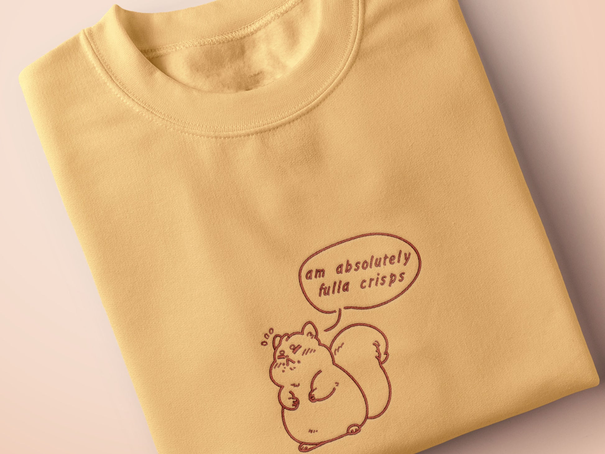An embroidered yellow t-shirt design of a cute fat chibi squirrel and a speech bubble with the text Am Absolutely Fulla Crisps from the drunken Scottish meme video.