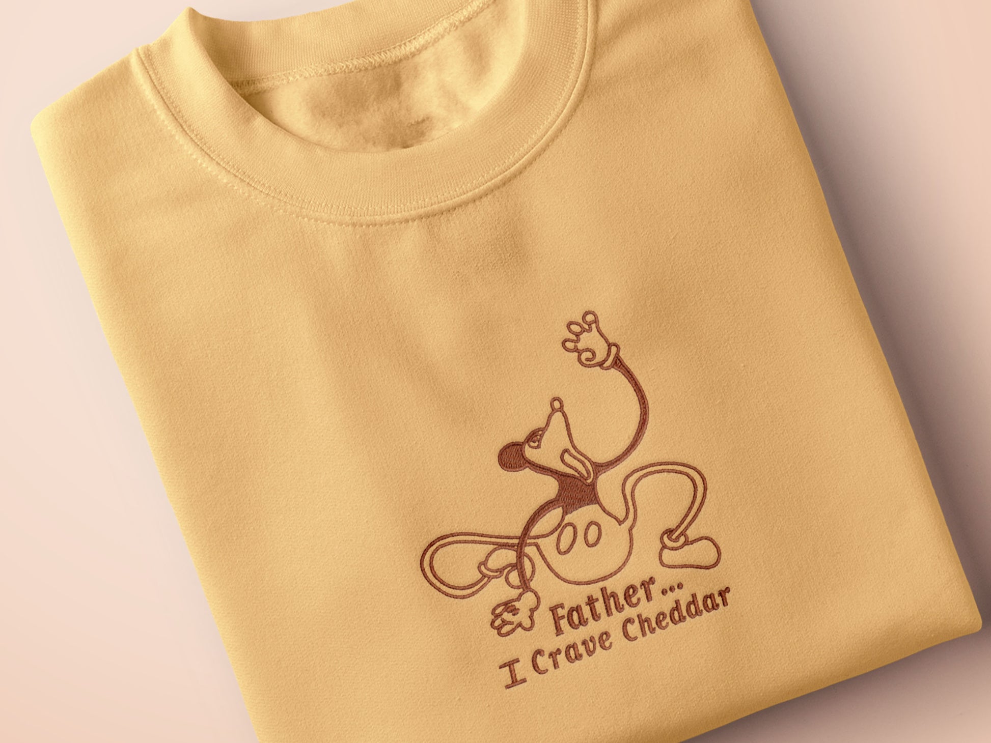 A yellow crew neck short sleeve t-shirt, with an embroidered black thread design of a mickey mouse like creature grasping the air with the text Father... I crave cheddar