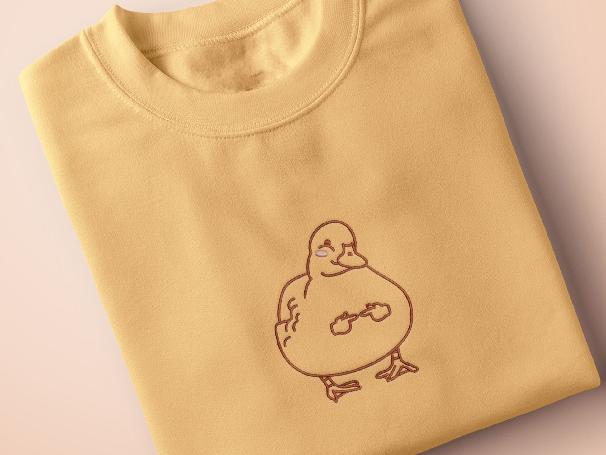 A yellow crew neck short sleeve t-shirt, with an embroidered black thread design of a cute blushing duck with the for me finger hand emoji symbols