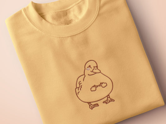 A yellow crew neck short sleeve t-shirt, with an embroidered black thread design of a cute blushing duck with the for me finger hand emoji symbols