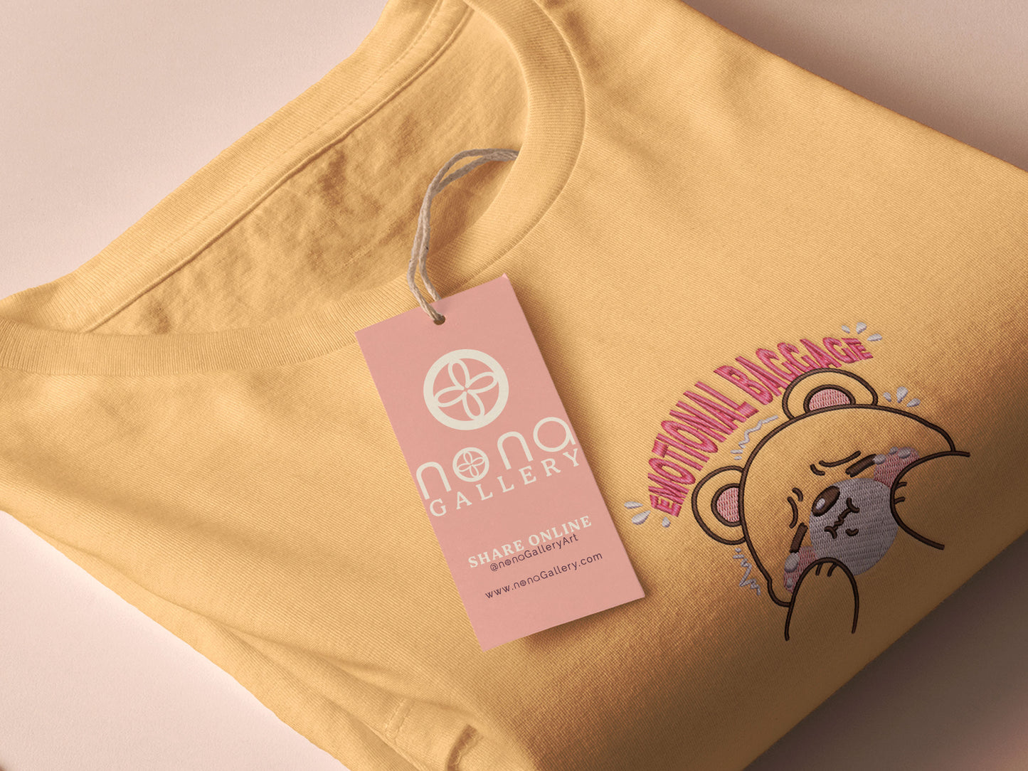 A yellow crew neck short sleeve t-shirt, with an embroidered brown thread design of a cute panicking bear and the quote emotional baggage
