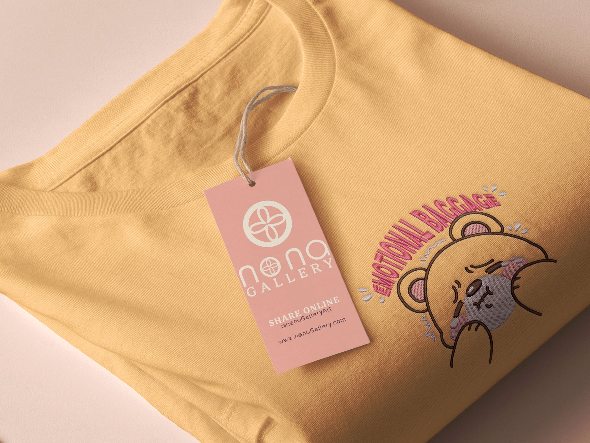 A yellow crew neck short sleeve t-shirt, with an embroidered brown thread design of a cute panicking bear and the quote emotional baggage